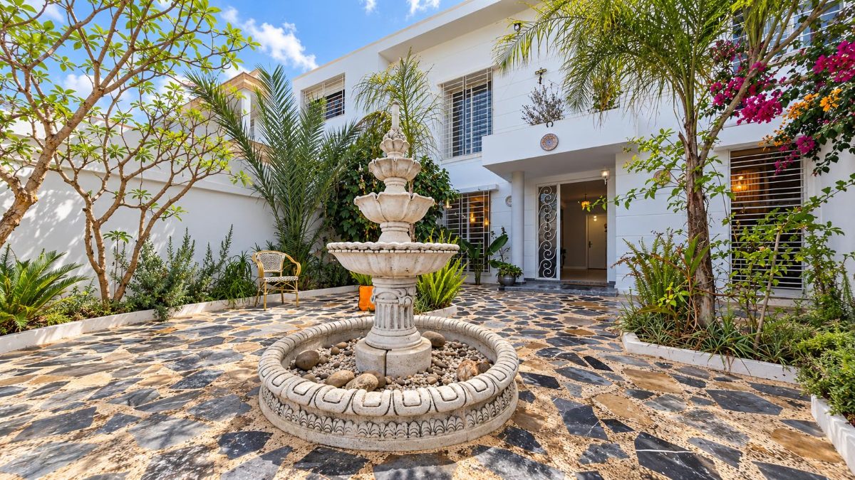 Villa à louer à Harhoura : cour avec fontaine, palmiers et façade blanche
